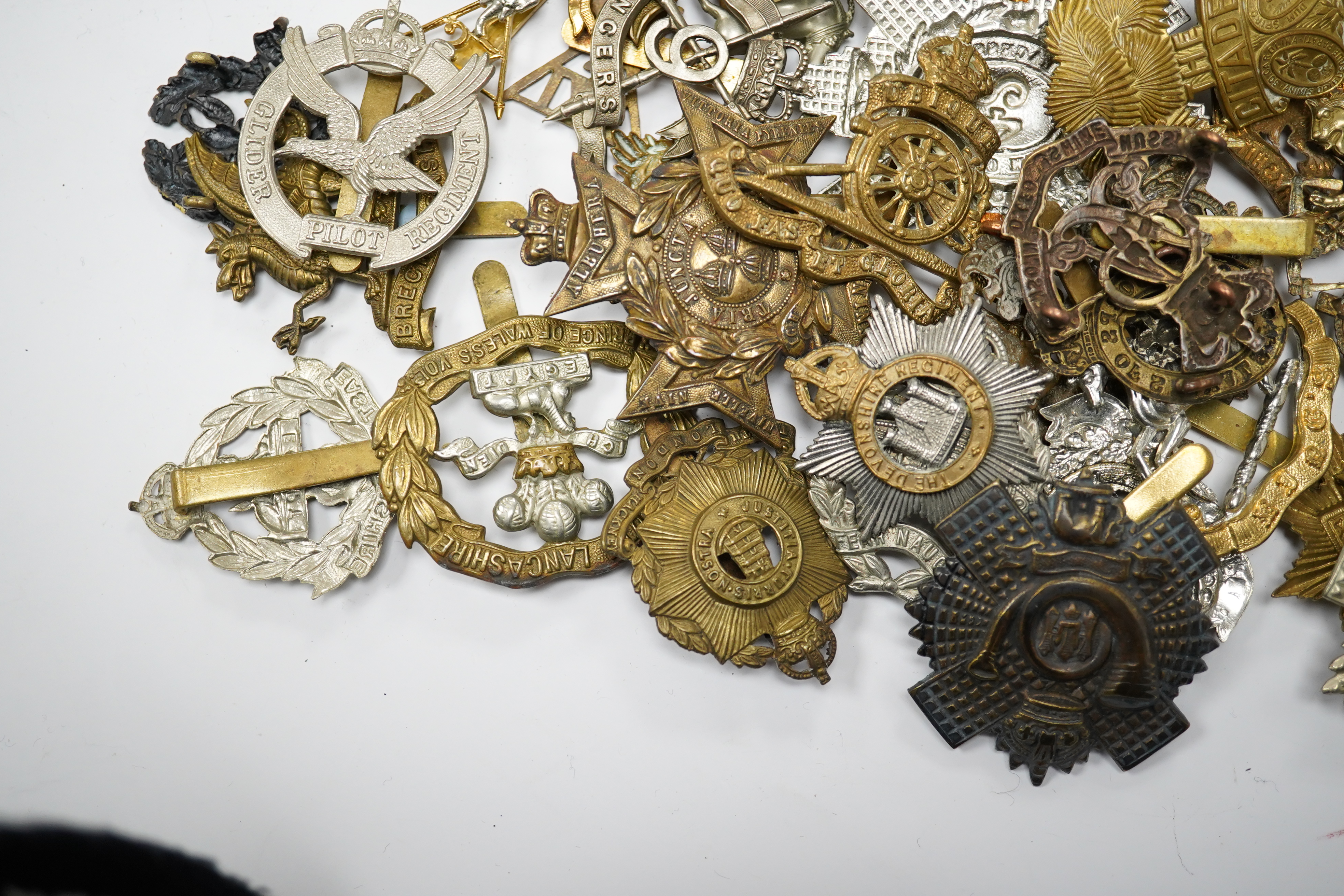 Sixty military cap badges, including; the Brecknockshire Regiment, the Royal Warwickshire Regiment, the South Lancashire Prince of Wales Volunteers, the Royal Artillery, the East Lancashire Regiment, the Glider Pilot Reg